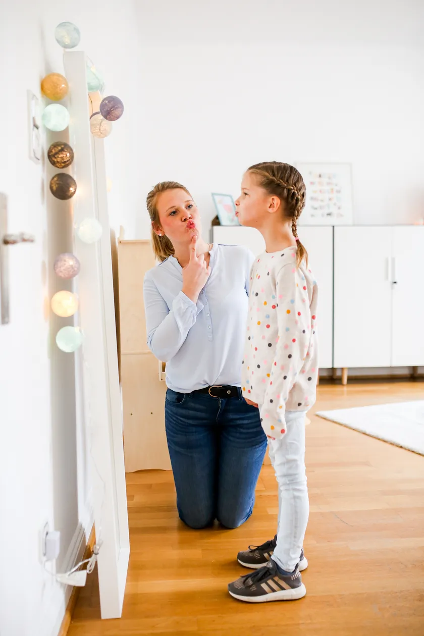 Eine Logopädin übt mit einem Mädchen vor dem Spiegel die Lautbildung