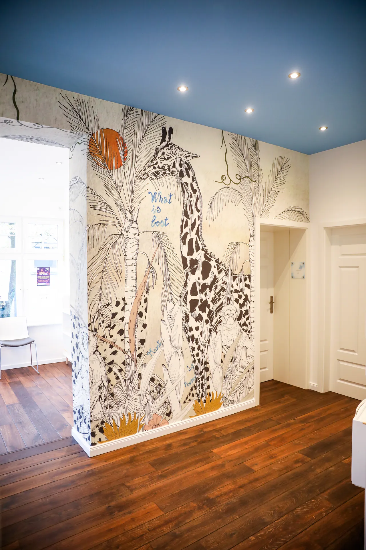 Am Ende des Flurs eine raumhoch gemalte Wand mit einer Giraffe zwischen gezeichneten Palmen