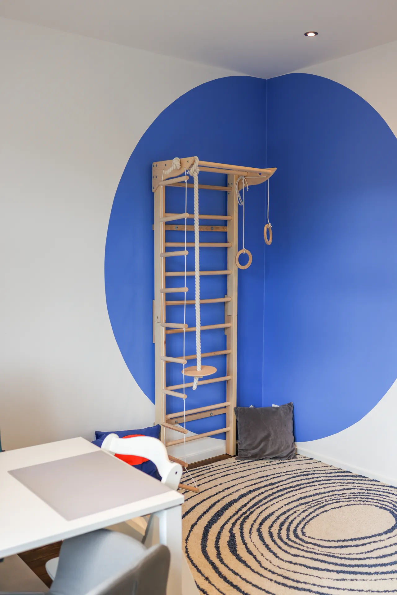 Therapieraum 3: eine hölzerne Sprossenwand vor einem großen blauen Wandkreis, davor ein Teppich mit rundem Muster und ein Tisch