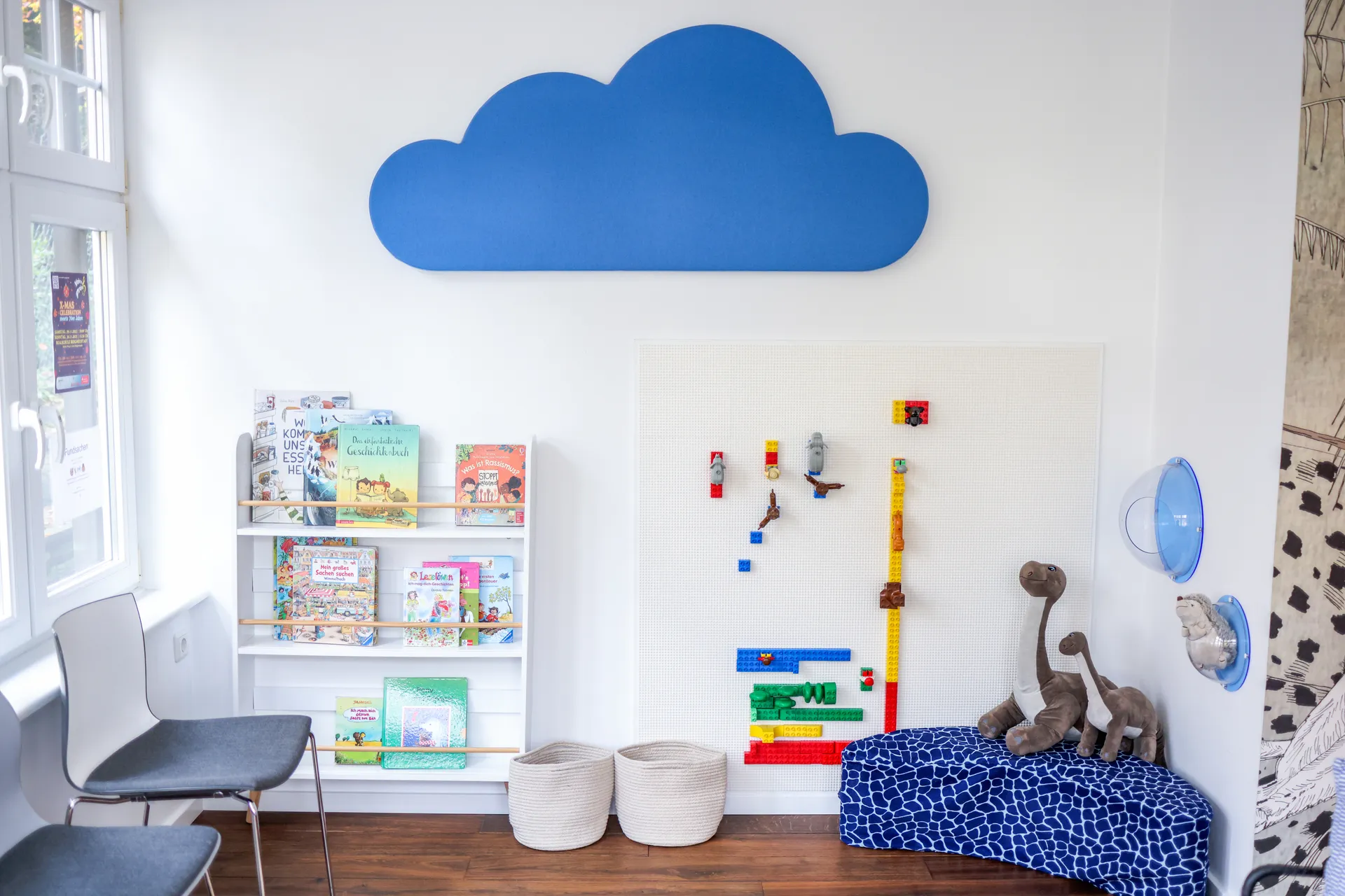 Die Kinderecke im Wartebereich: eine blaue Wolke an der Wand, ein Bücherregal und eine gepolsterte Sitzbank