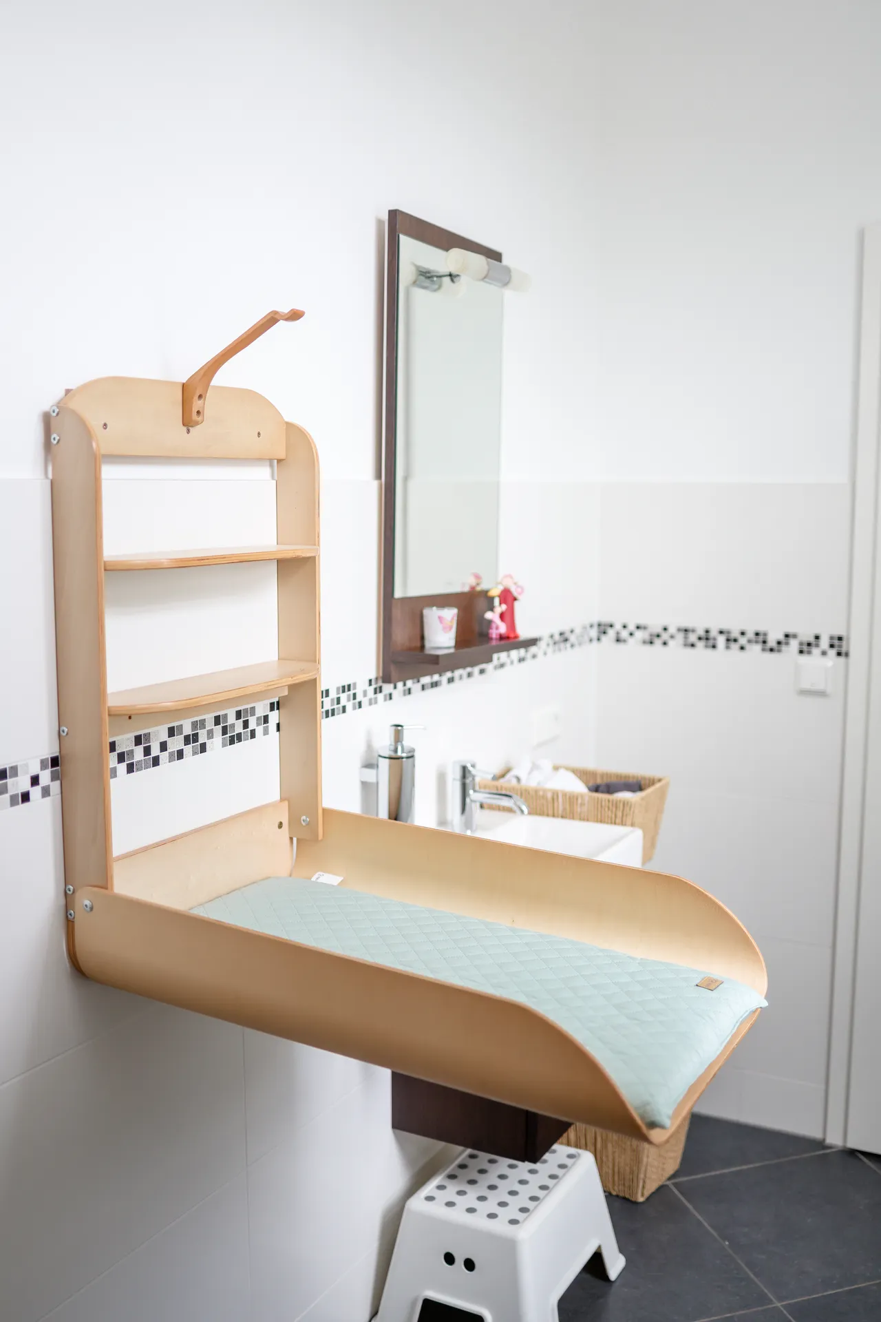 Der Wickelraum mit einem klappbaren Wickeltisch an der Wand, Spiegel und einem Tritthocker