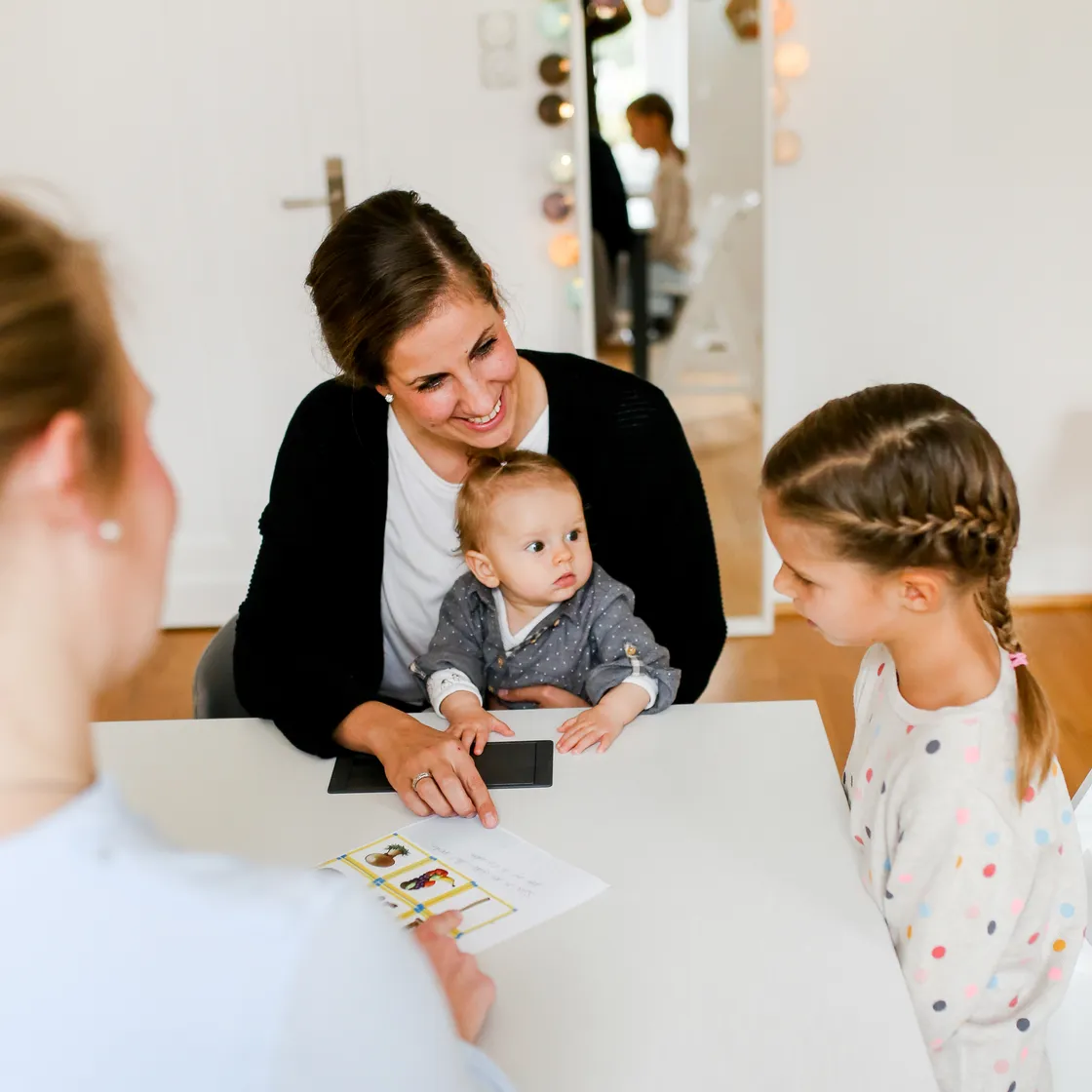 Eine Logopädin arbeitet mit zwei Kindern und einem Baby am Therapietisch